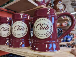 Red beer steins lined up on a plank of wood with brewery logo.