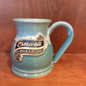 Blue coffee mug with the text "Creswell Bakery" in a clay logo medallion.