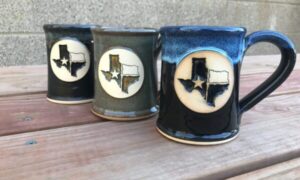 Three handmade coffee mugs with clay logo medallions featuring the outline of the state of Texas.
