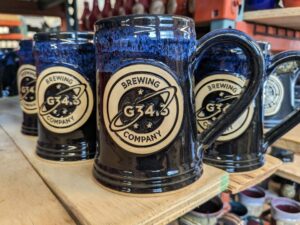 Black and blu beer steins on a wood plank with a custom logo medallion reading "g.34 brewing company".