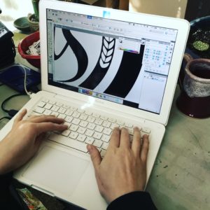 Up close view of two hands typing on a laptop computer with a large illustration on the screen.