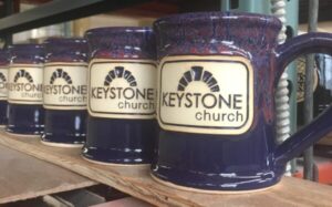Row of blue coffee mugs with a logo medallion with the text "Keystone Church".