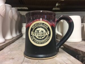 Black and red coffee mug with a clay medallion logo reading "Integrity Heating and Air Conditioning."