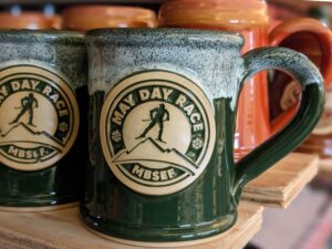 green coffee mugs with a logo of a figure skiing in a may day race