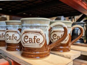brown and white coffees mugs on a shelf with the logo for 'abita springs cafe'