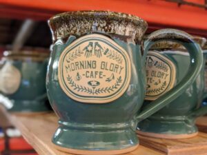 green and brown coffee mugs on a shelf with the logo for 'morning glory cafe'