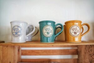white, teal and gold logo coffee mugs on a shelf