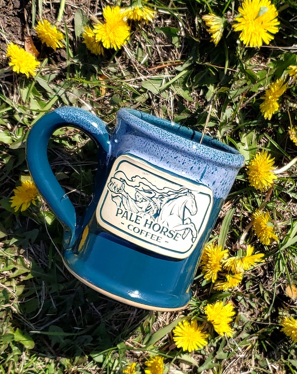 green pottery mug with a logo laying in a field of flowers